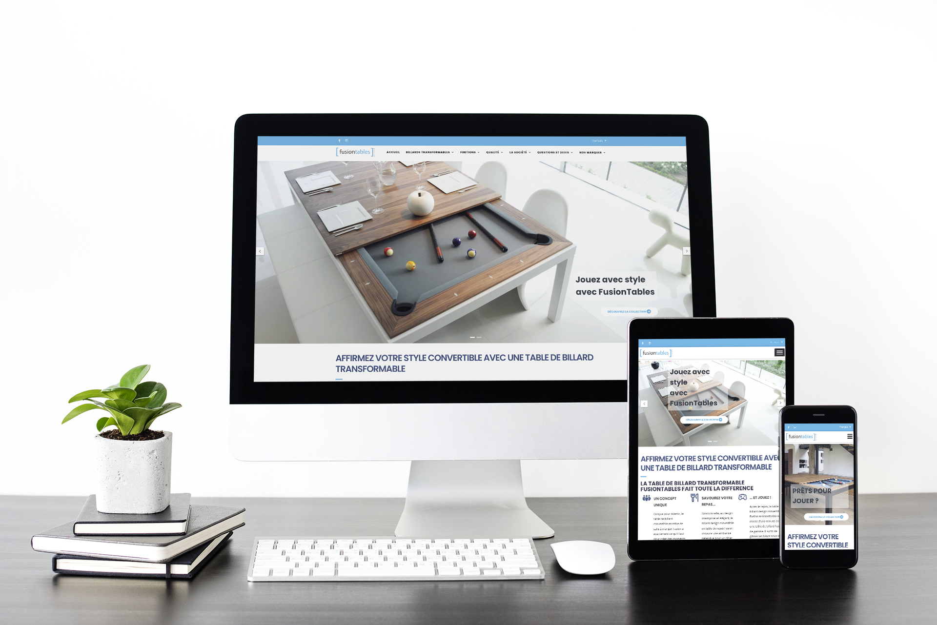 Un bureau moderne en bois avec un ordinateur de bureau, une tablette et un smartphone affichant un site web de tables de billard transformables, accompagné d'une petite plante en pot et de quelques carnets empilés.