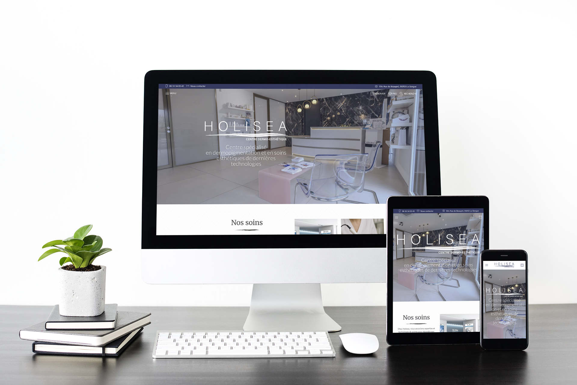 Un bureau moderne avec un ordinateur de bureau affichant le site web d'HOLISEA, un centre de soins esthétiques, accompagné d'une tablette et d'un smartphone avec le même site. Une plante en pot est posée sur des carnet noirs.