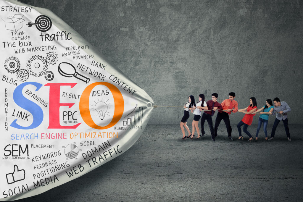 Un groupe de personnes tire sur une corde tandis qu'une bannière portant les mots "SEO" et "Search Engine Optimization" avec des éléments graphiques associés est présentée, symbolisant des concepts de marketing digital comme le trafic et les mots-clés, dans un environnement de bureau.